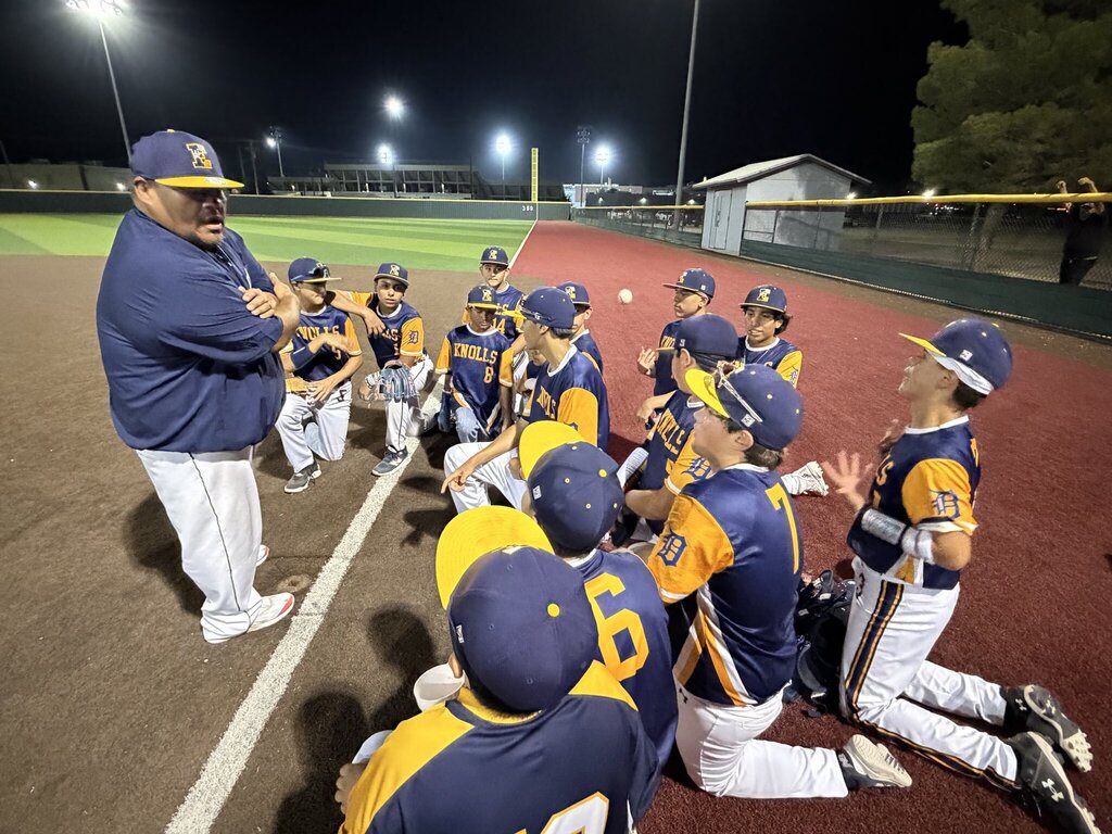Photo of the EKIS 8th grade baseball team huddled together listening to the coach.