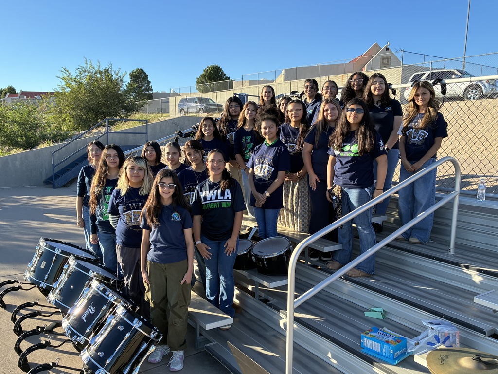 A group of students wearing YWLA shirts pose together on outdoor bleachers beside several marching drums.