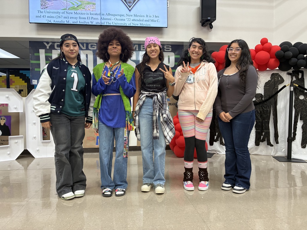 Alt text: Five students pose together in colorful, decade-inspired outfits during a school spirit event.