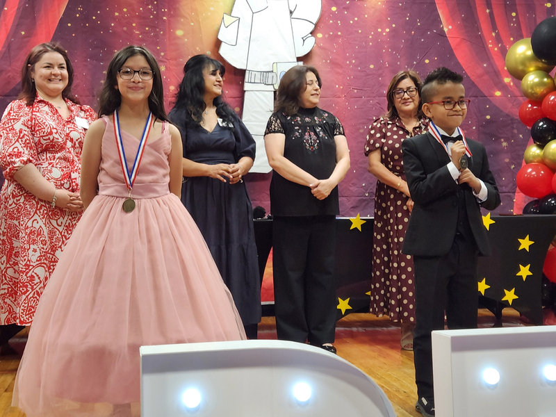 Two second grade students standing in front of their teachers after having received medals for their achievement in Reading