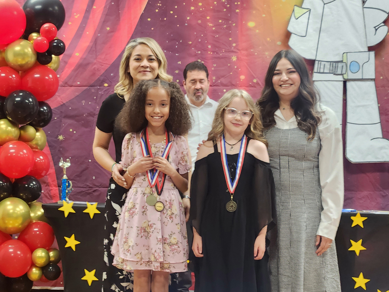 Third grade students wearing their medals and posing with their teachers on stage