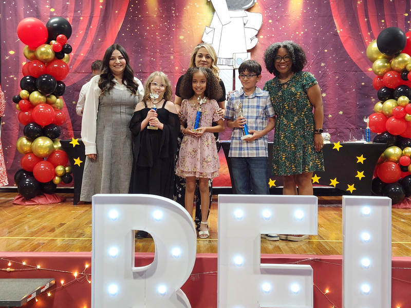 Third grade students holding their trophies and posing with their teachers on stage