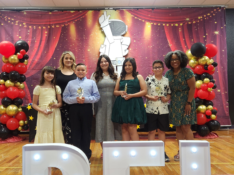 Third grade students holding their trophies and posing with their teachers on stage