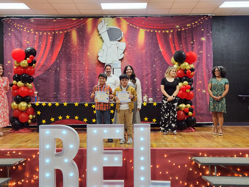 Third grade students holding their certificates and posing with their teachers on stage