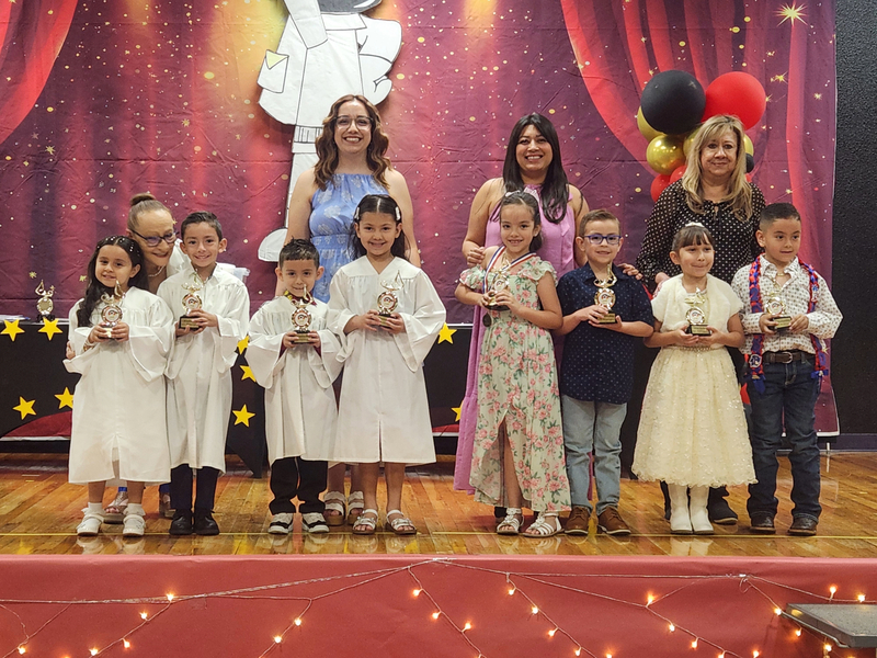 REL kinder teachers with their students on stage at the awards assembly