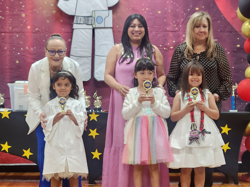 Teachers and 3 students posing on stage after receiving their trophies