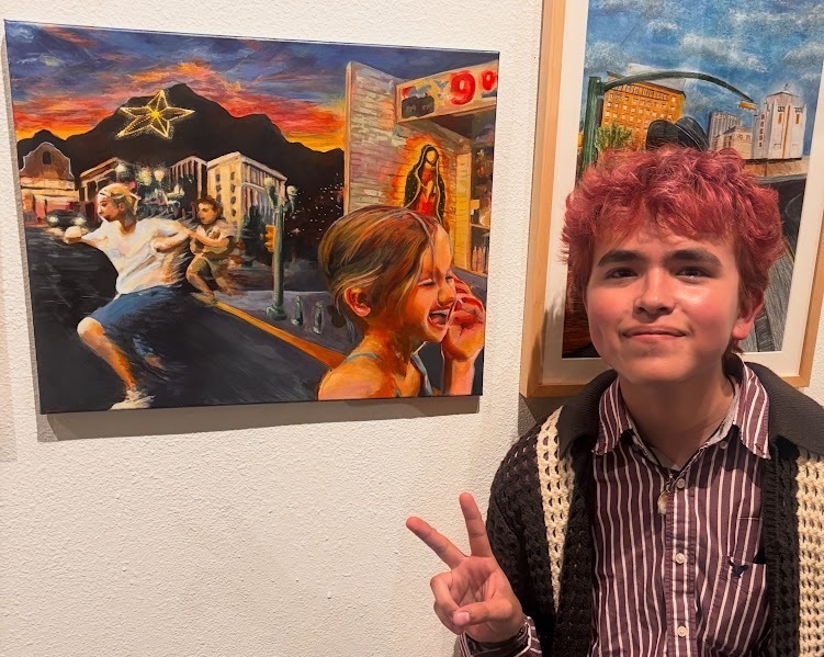 Art student, Giovanny Ortiz, stands beside his displayed artwork while displaying the peace sign with his right hand.