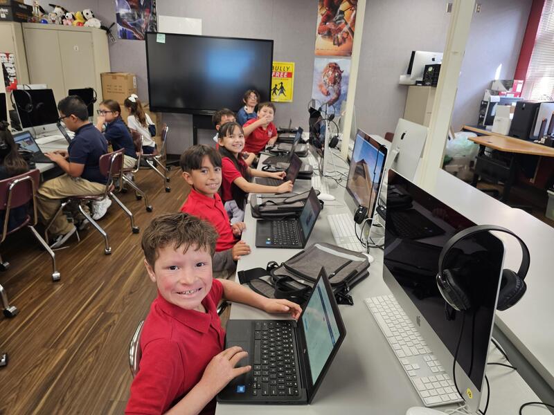 Group of 3rd graders sit with their Chromebooks working on Adobe Ai program and smile at the camera