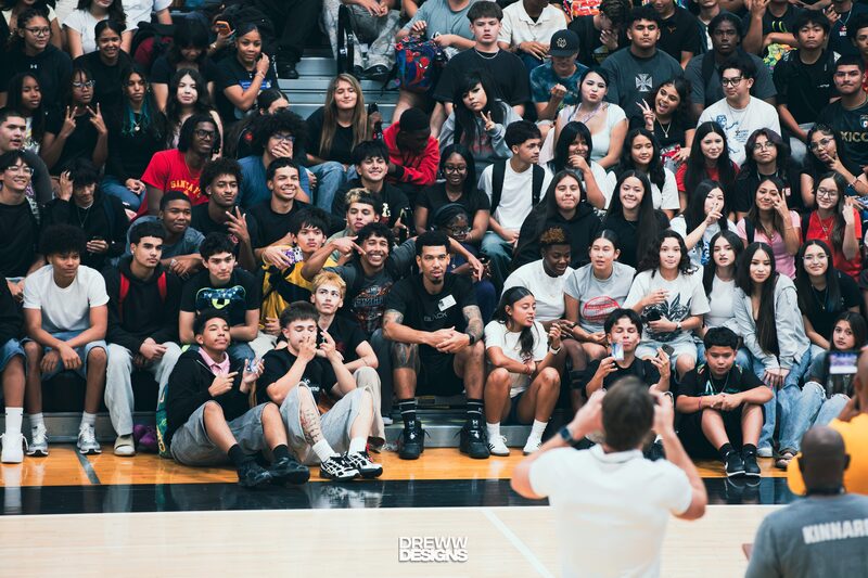 Danny Green sitting on bleachers filled with students posing for a picture.