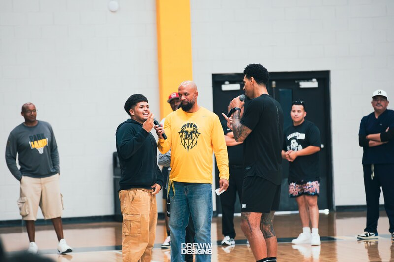 Parkland High School student holding a microphone, standing near Coach Vanley and Danny Green. Other coaches are standing in the background of the gym.