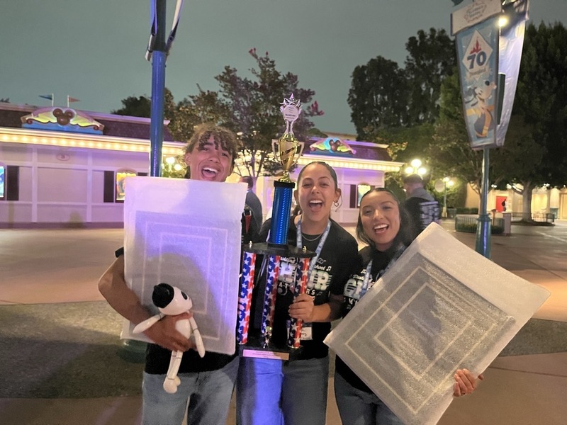 3 students are smiling and each holding an award from the competition.