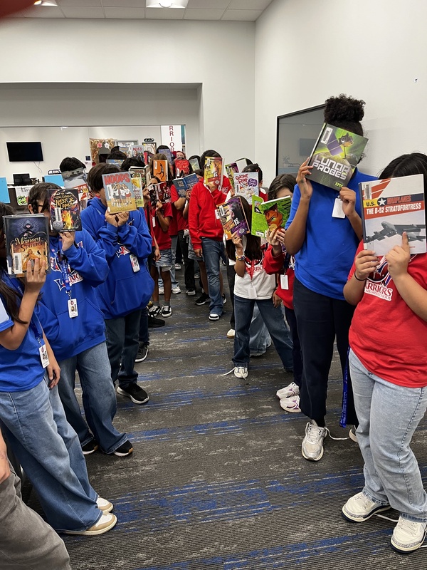 Students from Bookclub posing with a book covering their face to celebrate reading