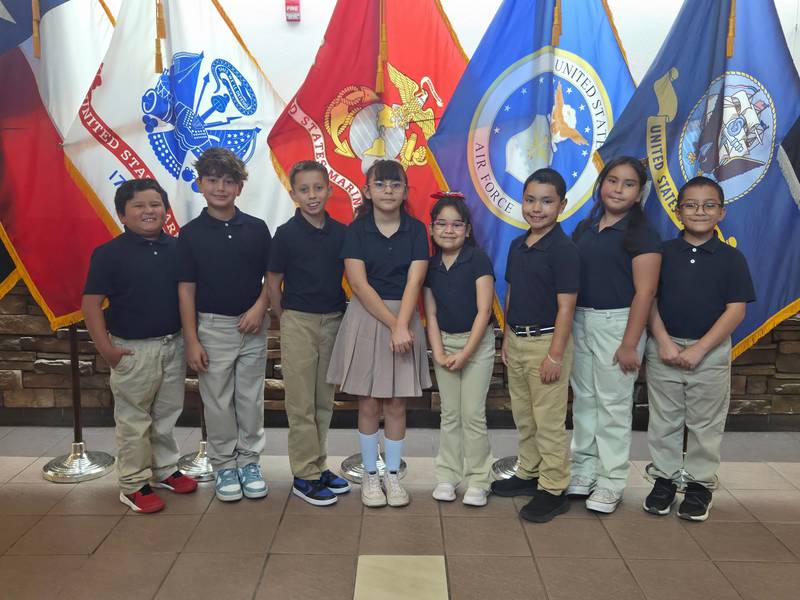 Presa Students pose in front of  multiple branches of military flags