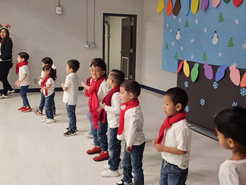 Ms. Avitia's PK class dances in their white t-shirts, jeans and red scarf on stage