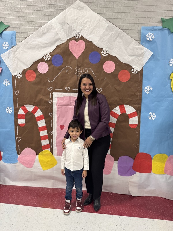Mom poses with PK son in front of Gingerbread house with candy canes