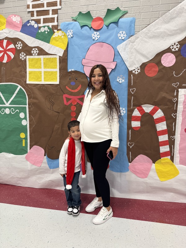 Pregnant Mom and her PK son with red scarf pose in front of Gingerbread backdrop