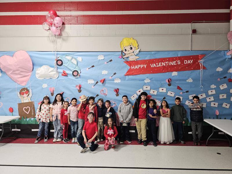 Ms. Reynoso's 3rd graders pose in front of the Happy Valentine's Day Angel Back drop