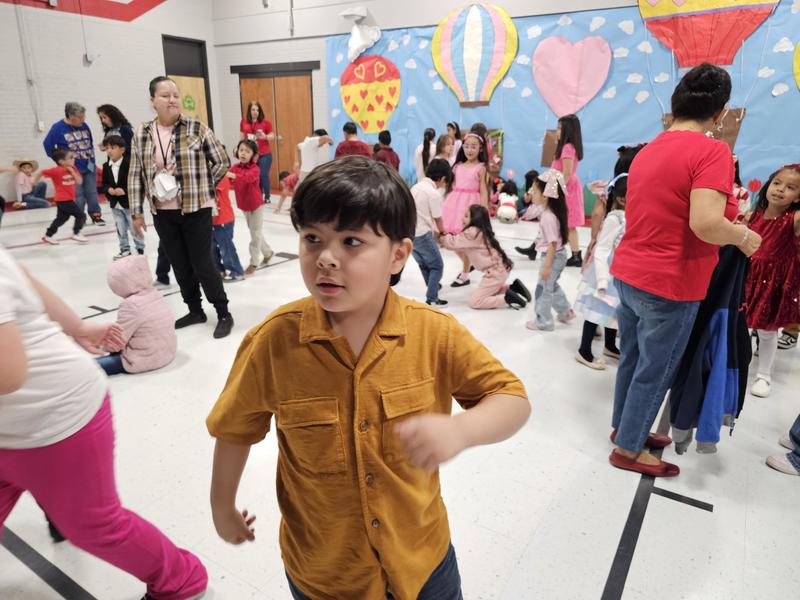 Student in a mustard colored shirt dances with students and teachers in the background