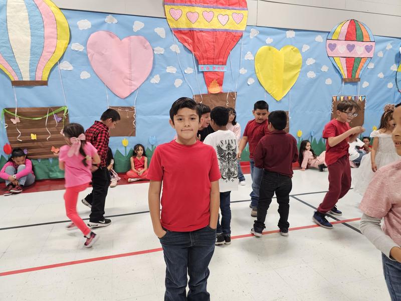 4th grader in red shirt stands with his hands in his pocket for a quick pic