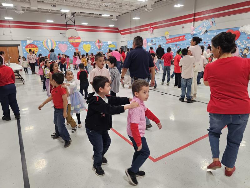 Kinder students make a line and dance around the floor.