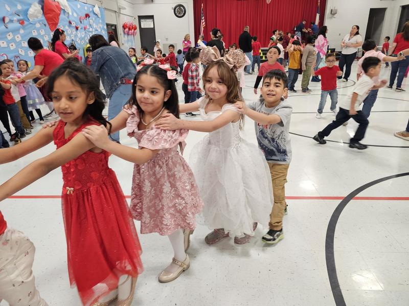 2nd grader girls in dresses and 1 boy make a line to dance around 