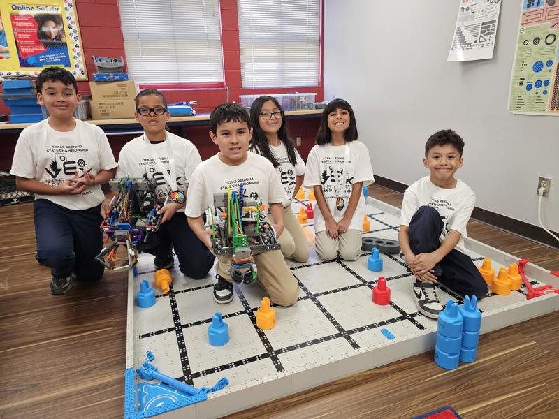 Both teams sit and pose on the field back at campus on Monday with Championship shirts and medals and robots