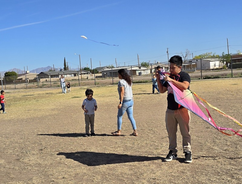 A Father working on his child's kite before flight while a Mom and her son are in the background