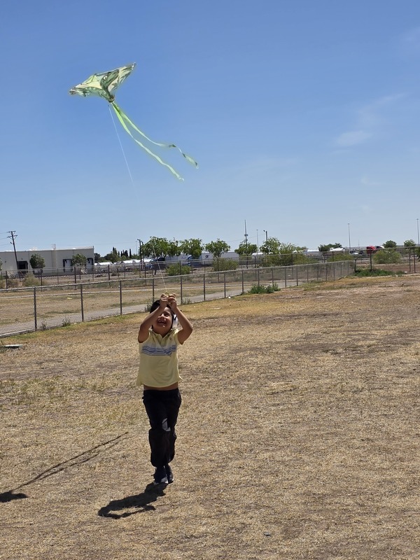 Young boy running with a kite toward the camera while his yellow kite flies in the sky behind him