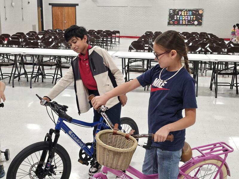 5th grade boy and 4th grade girl from left to right straddle their new bikes and admire them