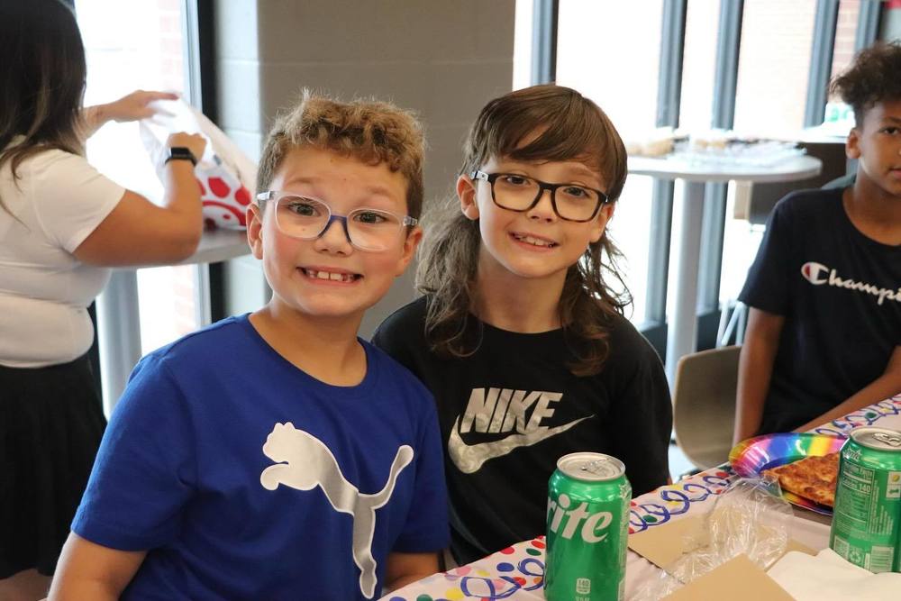 2 boys smiling in a cafeteria with their lunches