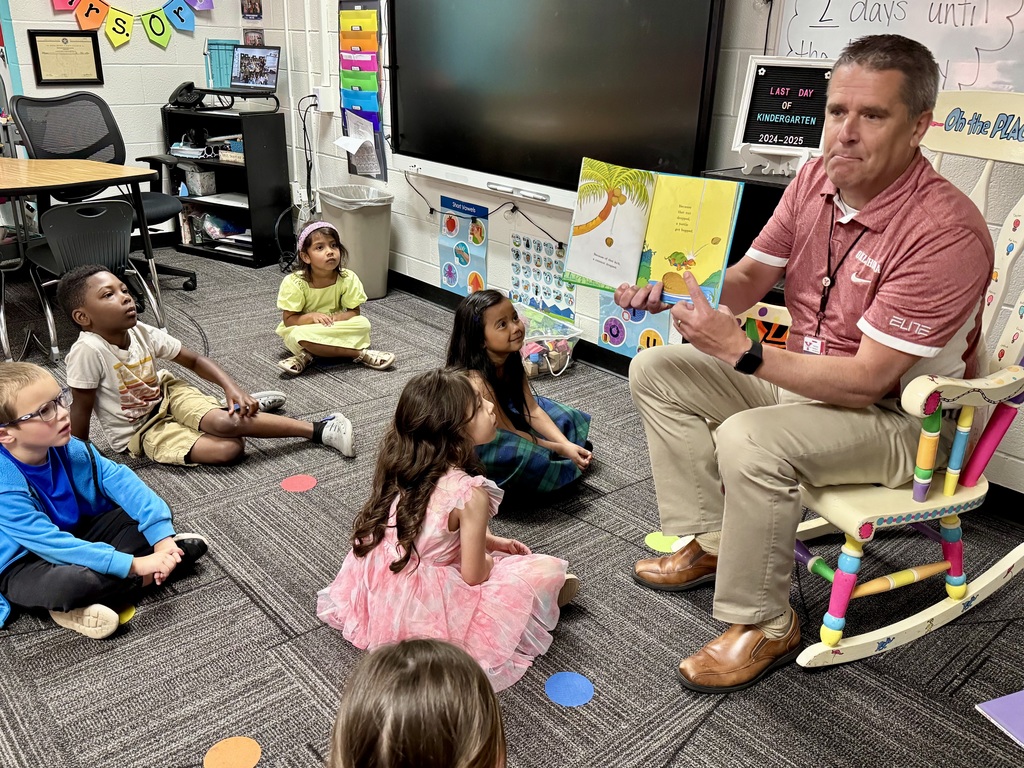 Man in a red shirt holding a book out for children to see