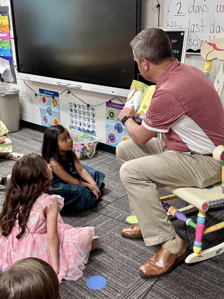 Man in a red shirt holding a yellow book out for kids to see the page