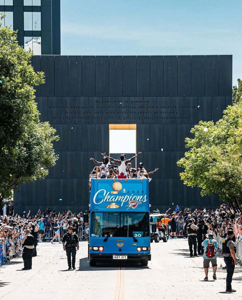 a blue bus with a championship title and gold basketball driving down the road with basketball players standing on top with their hands up
