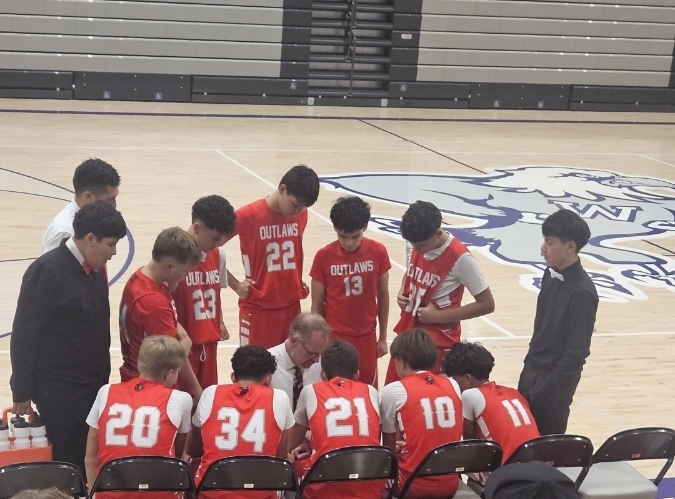 Team members in red jerseys huddle on a basketball court. Numbers on jerseys range from 10 to 34.